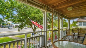 A covered porch with a view of a street, a flag, and a hot tub. - Serendipity | Classic Chincoteague Home Walk to Main Street w/ Screened Porch & First-Floor Bedroom (Chincoteague Island)