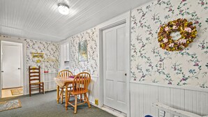 A room with floral wallpaper, a wooden dining table with chairs, a blue sofa, and a white door. - Serendipity | Classic Chincoteague Home Walk to Main Street w/ Screened Porch & First-Floor Bedroom (Chincoteague Island)