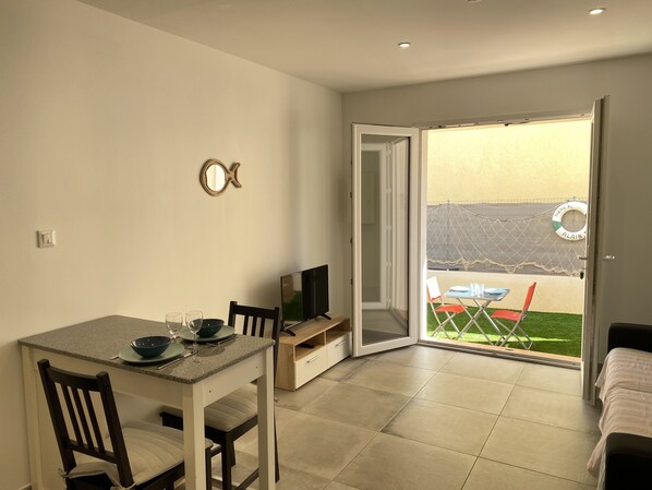 A dining area with a table, chairs, and a television. There is a sliding door leading to an outdoor space with a hammock and a pool.