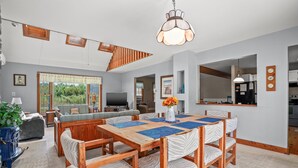 A spacious dining area with a wooden table and chairs, a chandelier, and a view of the outdoors. - Shady Side | Piney Island Home Near Beach w/ Community Water Access, Large Porch, Grill & Loft (Chincoteague Island)