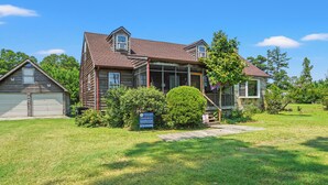 A two-story house with a front porch, a garage, and a well-maintained lawn. - Shady Side | Piney Island Home Near Beach w/ Community Water Access, Large Porch, Grill & Loft (Chincoteague Island)