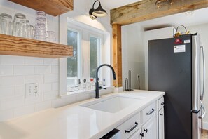 A kitchen with a white countertop, a black sink, and a stainless steel refrigerator.