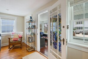 A room with a wooden rocking chair, a metal shelf with decorative items, and a door with stained glass.