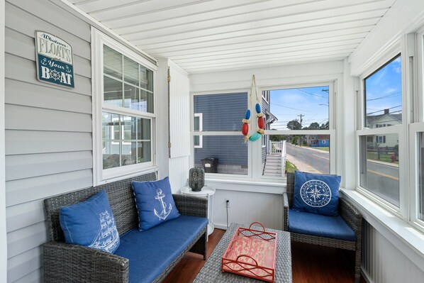 A covered porch with wicker furniture, a decorative sign, and a view of the street.