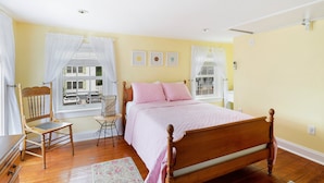 Un dormitorio con cama de madera, una silla, una mesita y una ventana con cortinas.