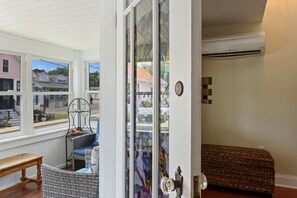 A room with a large window, a wicker chair, a wooden bench, and a door with a glass panel.