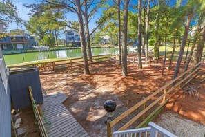 A deck with a grill, a dock, and a view of a lake and buildings. - Sunshine Daydream | Oyster Bay Canal Waterfront w/ Multiple Porches, Water Views & Dog Friendly (Chincoteague Island)