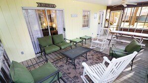 Uma área de estar coberta ao ar livre com cadeiras verdes e brancas, uma mesa e uma placa com a inscrição 'Boardwalk'.