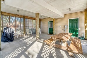 A covered patio area with a picnic table, chairs, and a green door. - Wildflower | Waterfront w/ Shared Pier & Floating Dock, Screened Porches + Balcony Views (Chincoteague Island)
