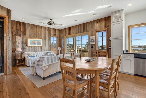 A cozy room with a wooden floor, a dining table with chairs, a sofa, and a window with a view.