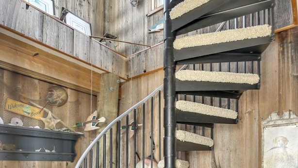 A spiral staircase with a wooden finish and a cat tree attached to the wall. - Wildflower | Waterfront w/ Shared Pier & Floating Dock, Screened Porches + Balcony Views (Chincoteague Island)