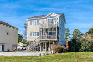 A two-story house with a balcony, a garage, and a driveway. - Wildflower | Waterfront w/ Shared Pier & Floating Dock, Screened Porches + Balcony Views (Chincoteague Island)