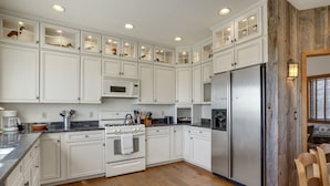 A kitchen with white cabinetry, a stainless steel refrigerator, a microwave, and a stove. - Wildflower | Waterfront w/ Shared Pier & Floating Dock, Screened Porches + Balcony Views (Chincoteague Island)