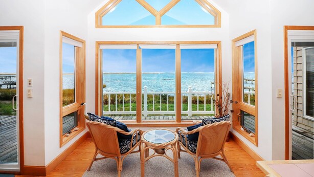A room with large windows, wicker chairs, a small table, and a view of the water.