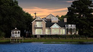 A two-story house with a balcony and a dock extending into a body of water.