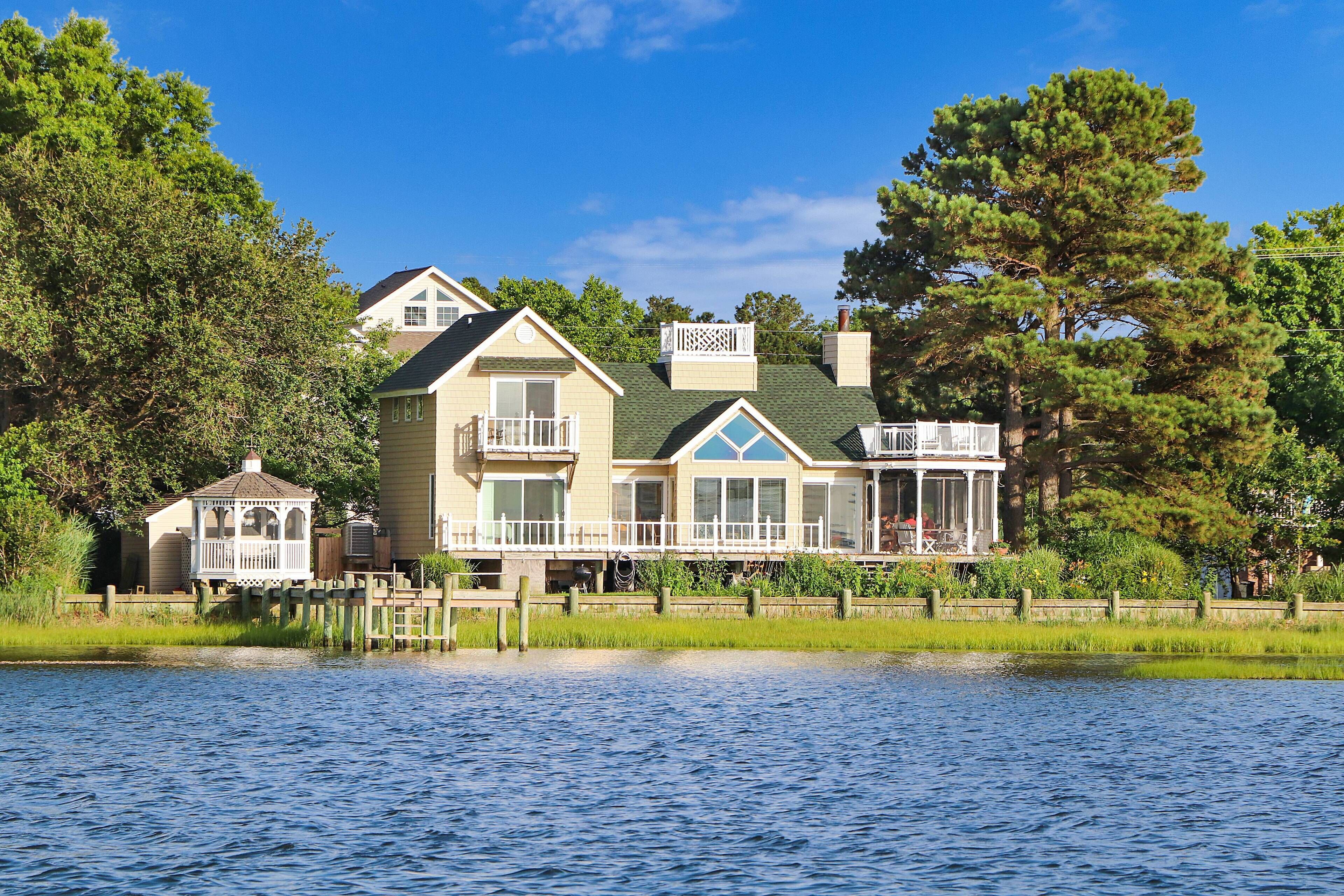 A large house with a dock extending into a lake, surrounded by trees.
