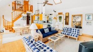 A spacious living area with a staircase, a sofa set, a dining table, and a kitchen in the background.
