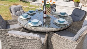 A round glass table set for six with wicker chairs, a bottle of wine, and a vase with tulips. - Bodwena (Moelfre)
