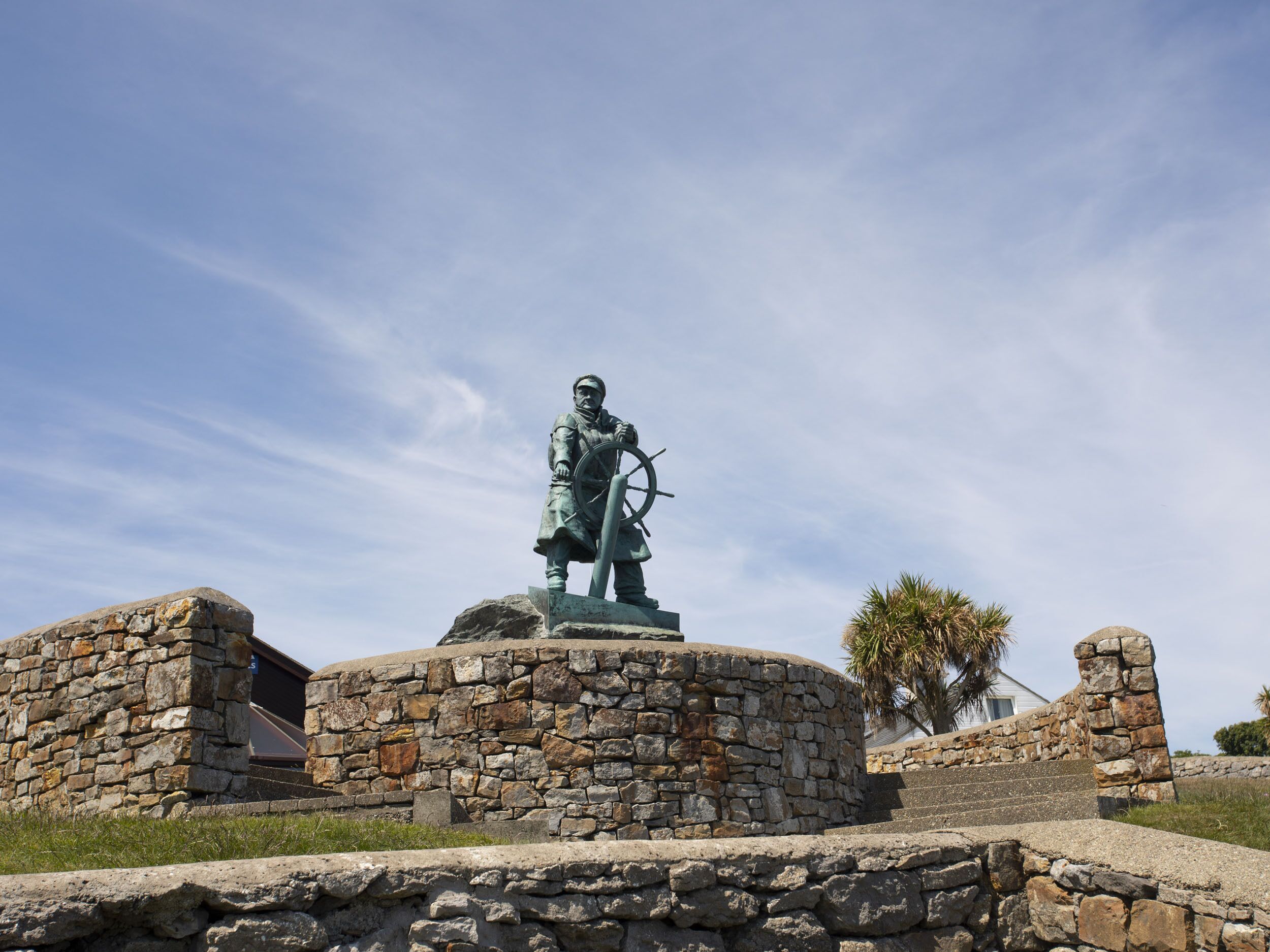 A statue of a historical figure on a stone pedestal with a stone wall and steps leading up to it.