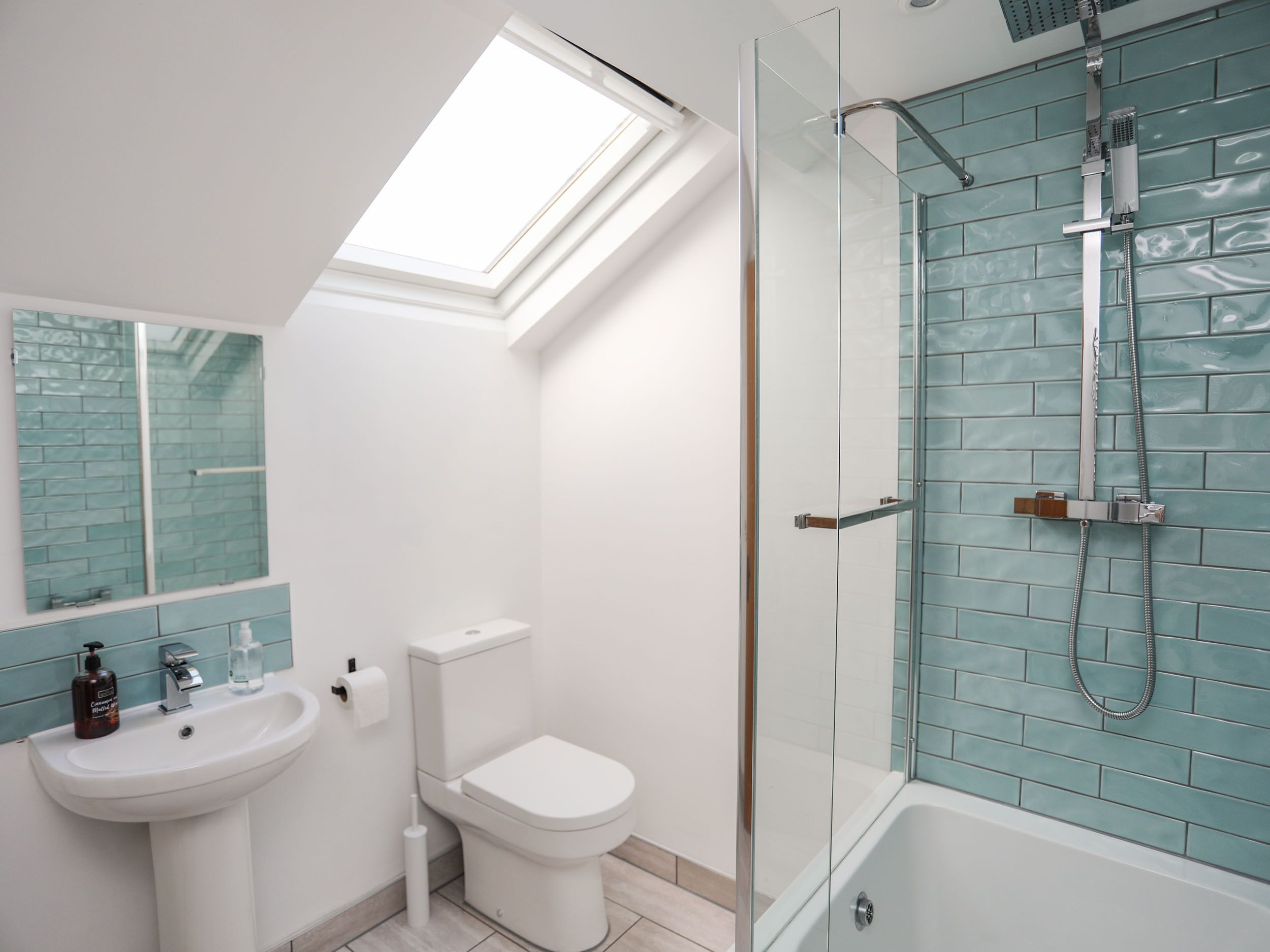 Un baño moderno con tragaluz, cabina de ducha de vidrio, lavabo blanco y retrete.