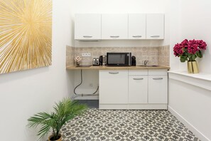 A compact kitchen with white cabinets, a microwave, and a coffee maker. There is a small potted plant and a vase with flowers on the counter. - Family Suite - Marais - Martin III (Paris)