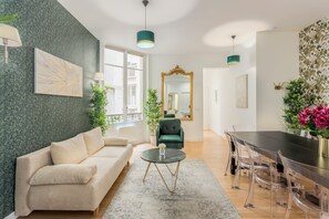 A living room with a sofa, a dining table with chairs, a mirror, and a window.