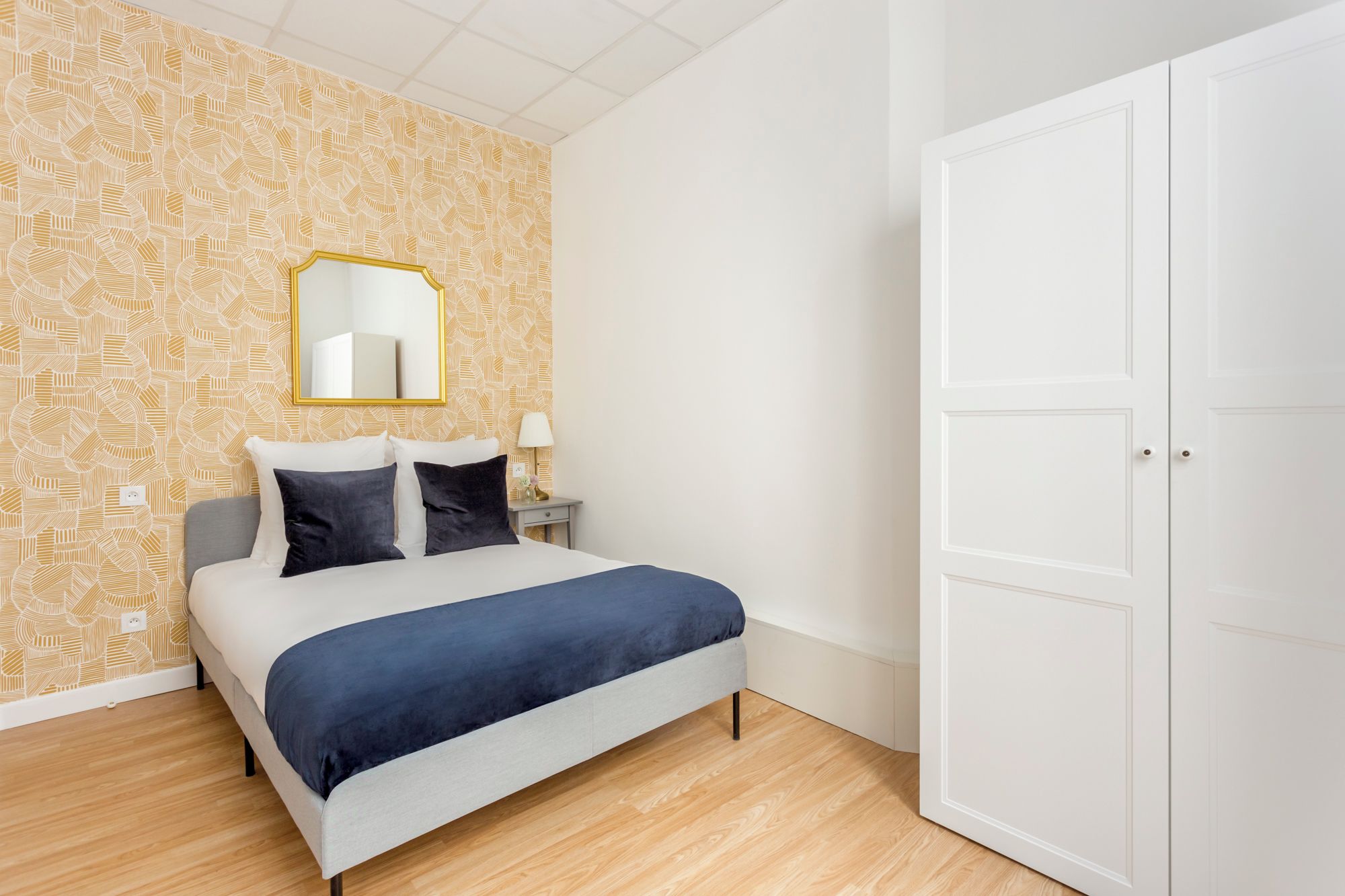 Ein Schlafzimmer mit einem Bett, einem Nachttisch, einer Lampe, einem Spiegel und einem Kleiderschrank.