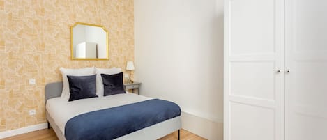 A bedroom with a bed, a nightstand, a lamp, a mirror, and a wardrobe.
