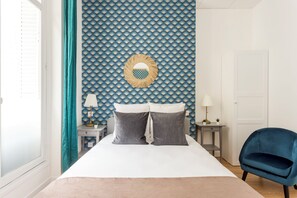 A bedroom with a bed, two bedside tables, a blue chair, and a patterned wall. - Family Suite - Marais - Martin III (Paris)