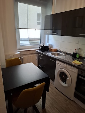 A compact kitchen with a washing machine, a sink, and a window.