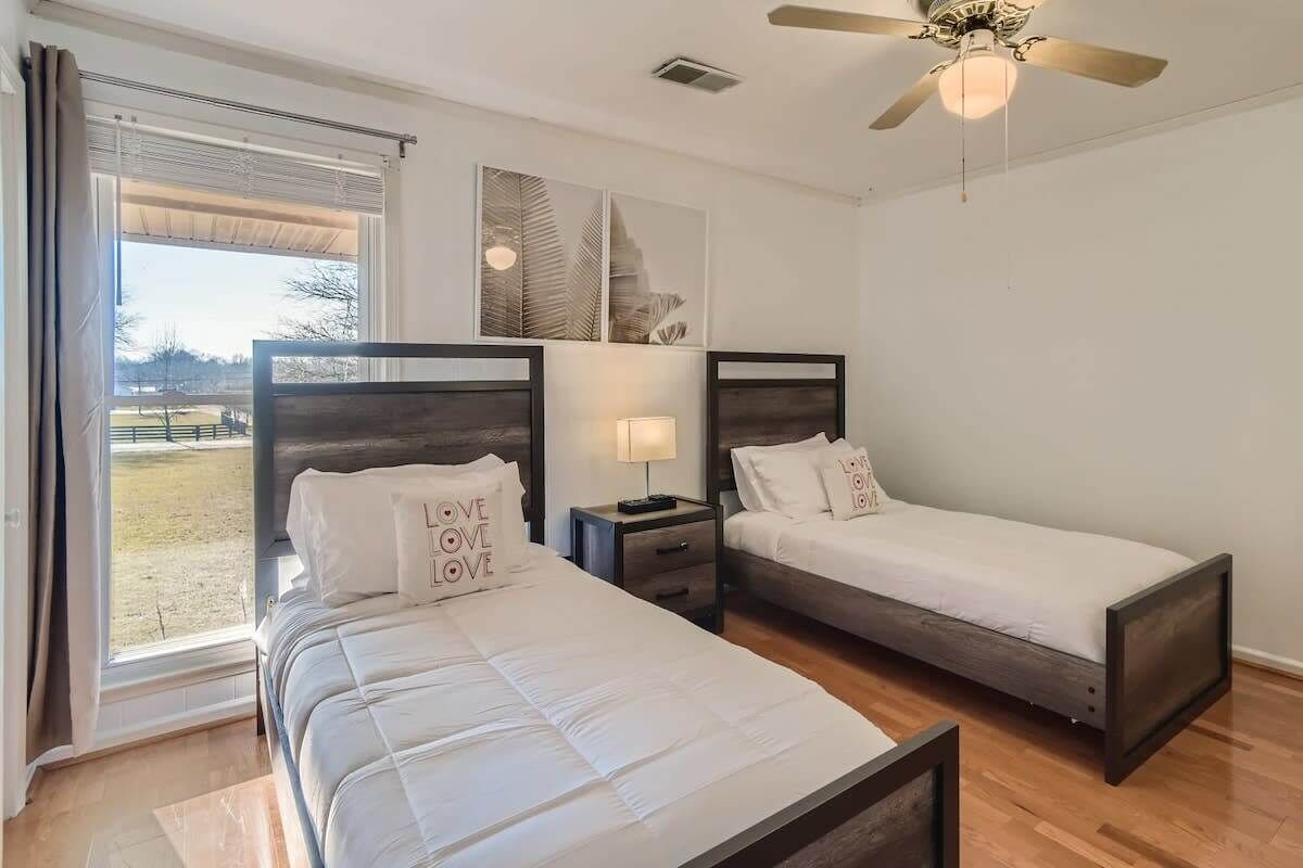 A bedroom with two beds, a ceiling fan, and a window with curtains.