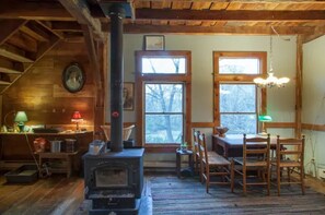Cozy retreat with a central wood-burning stove, wooden ceiling, and large window overlooking the surrounding trees.