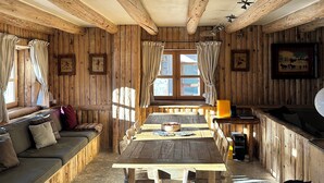 Un intérieur rustique en bois, avec une longue table à manger, des sièges rembourrés et une fenêtre agrémentée de rideaux.
