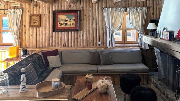 L’intérieur d’un chalet rustique, avec des murs en bois, un canapé, une table en bois et une cheminée.