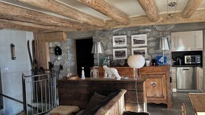 Une cuisine rustique avec des poutres en bois, un mur en pierre et un coin repas comprenant un banc et une table en bois.