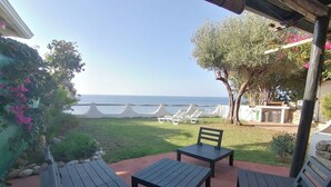 An outdoor patio with wooden tables and chairs, a view of the sea, and a garden with flowers and trees. - Costa dei monaci Villas - Tropea (PARGHELIA)
