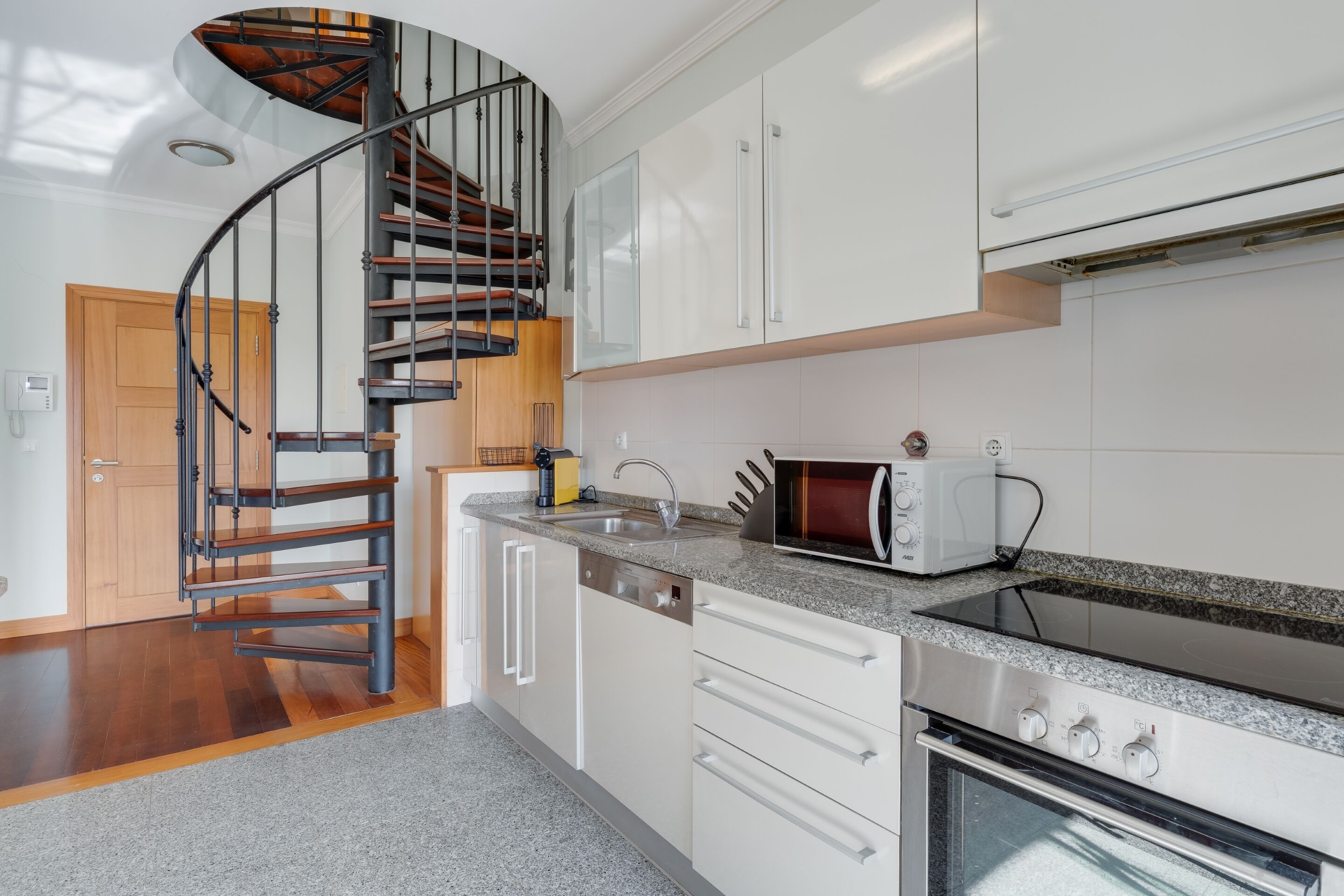 A modern kitchen with a spiral staircase, white cabinetry, a built-in oven, and a microwave.