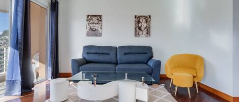 Una sala de estar moderna con un sofá azul, un sillón amarillo y una mesa de centro de vidrio.