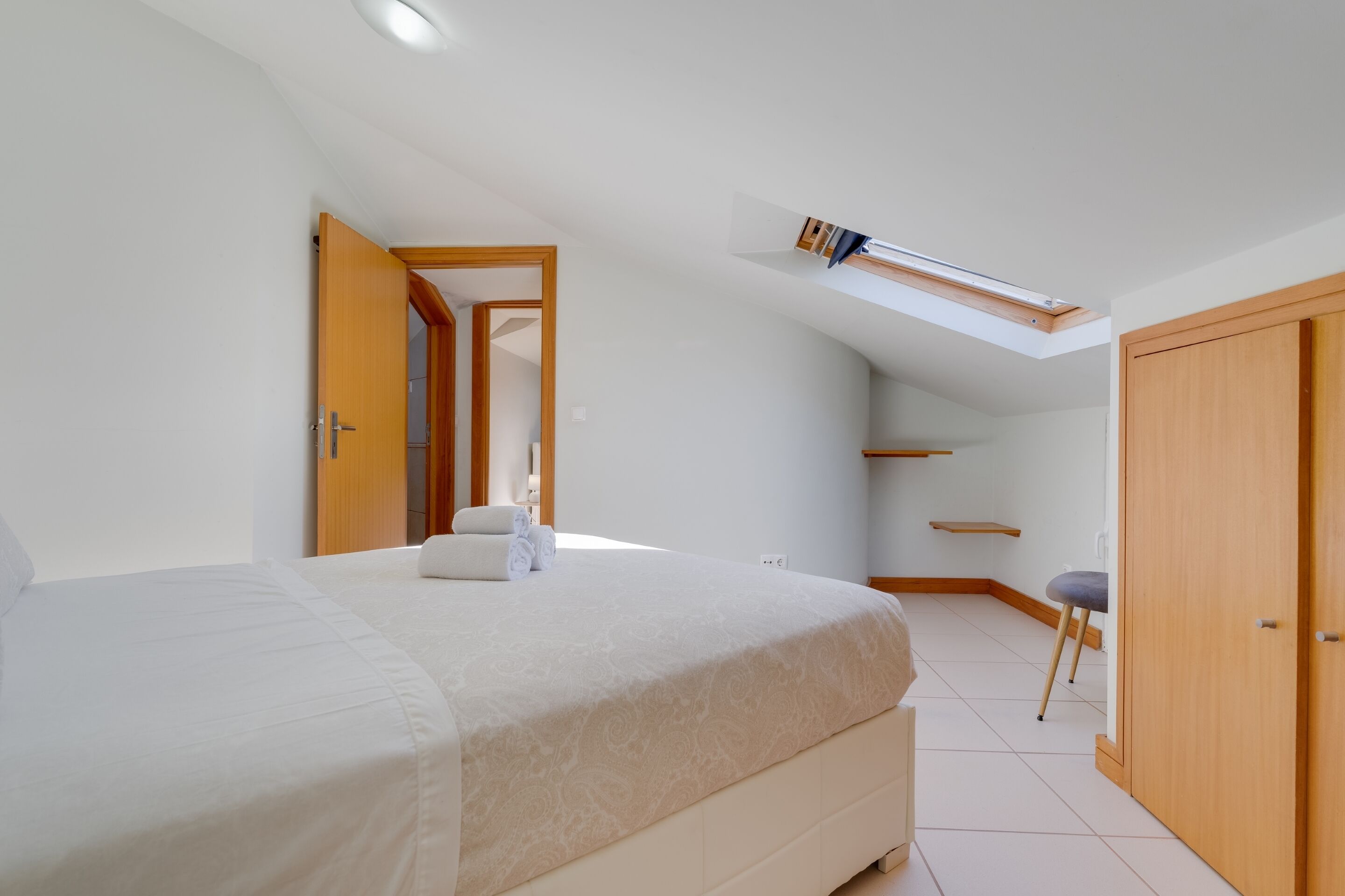 A bedroom with a bed, a skylight, a wardrobe, and a small stool.