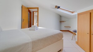 Una camera da letto con un letto, una finestra a lucernario, un armadio e uno sgabello.