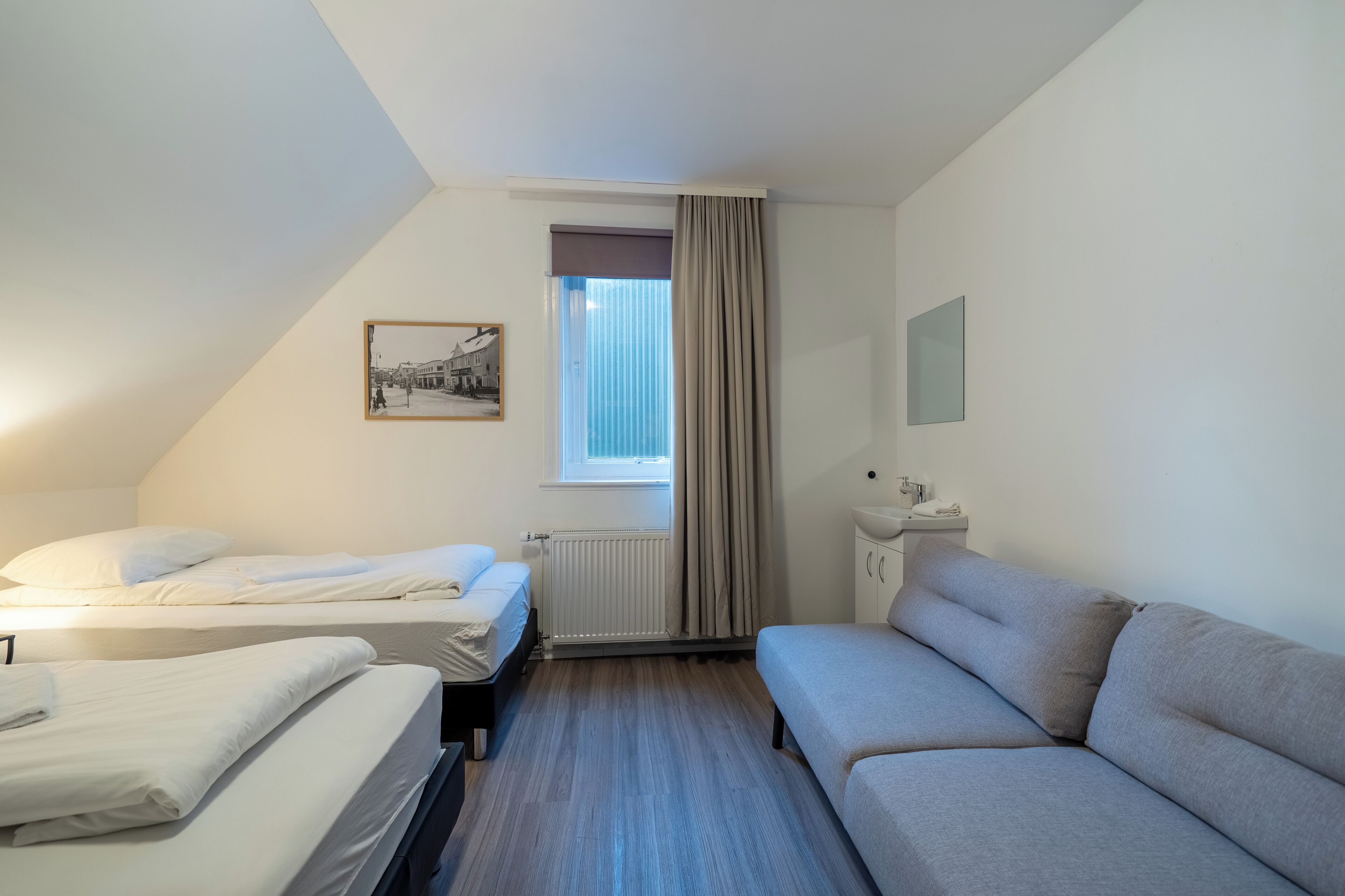 Une chambre avec deux lits, un canapé, une fenêtre avec des rideaux, un radiateur et une petite table avec une lampe.