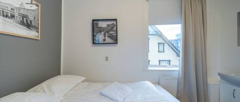 Une chambre d’hôtel avec un lit, une fenêtre avec des rideaux, un tableau accroché au mur et un radiateur.