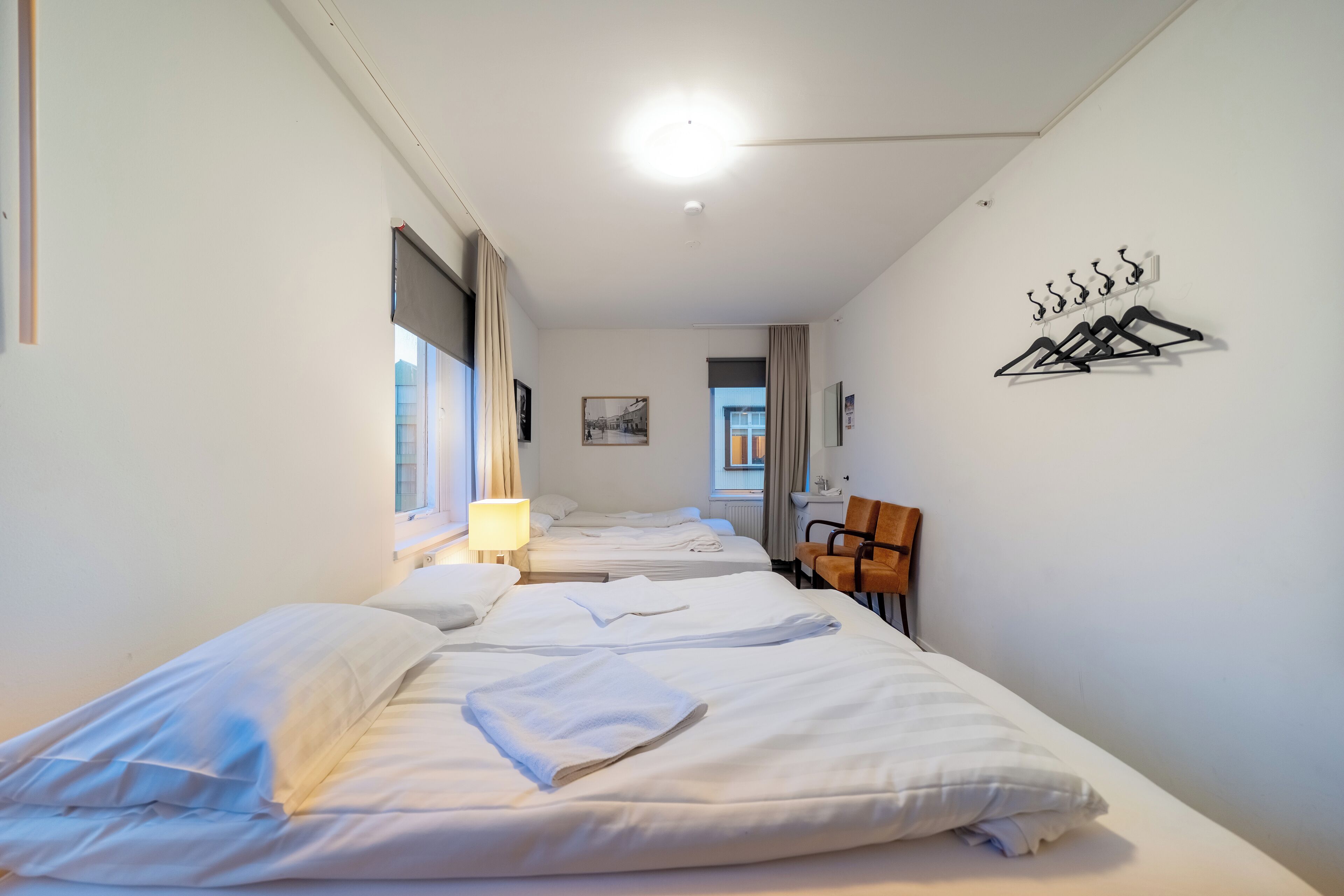 Habitación de hotel con tres camas, una silla, perchero y lámpara.