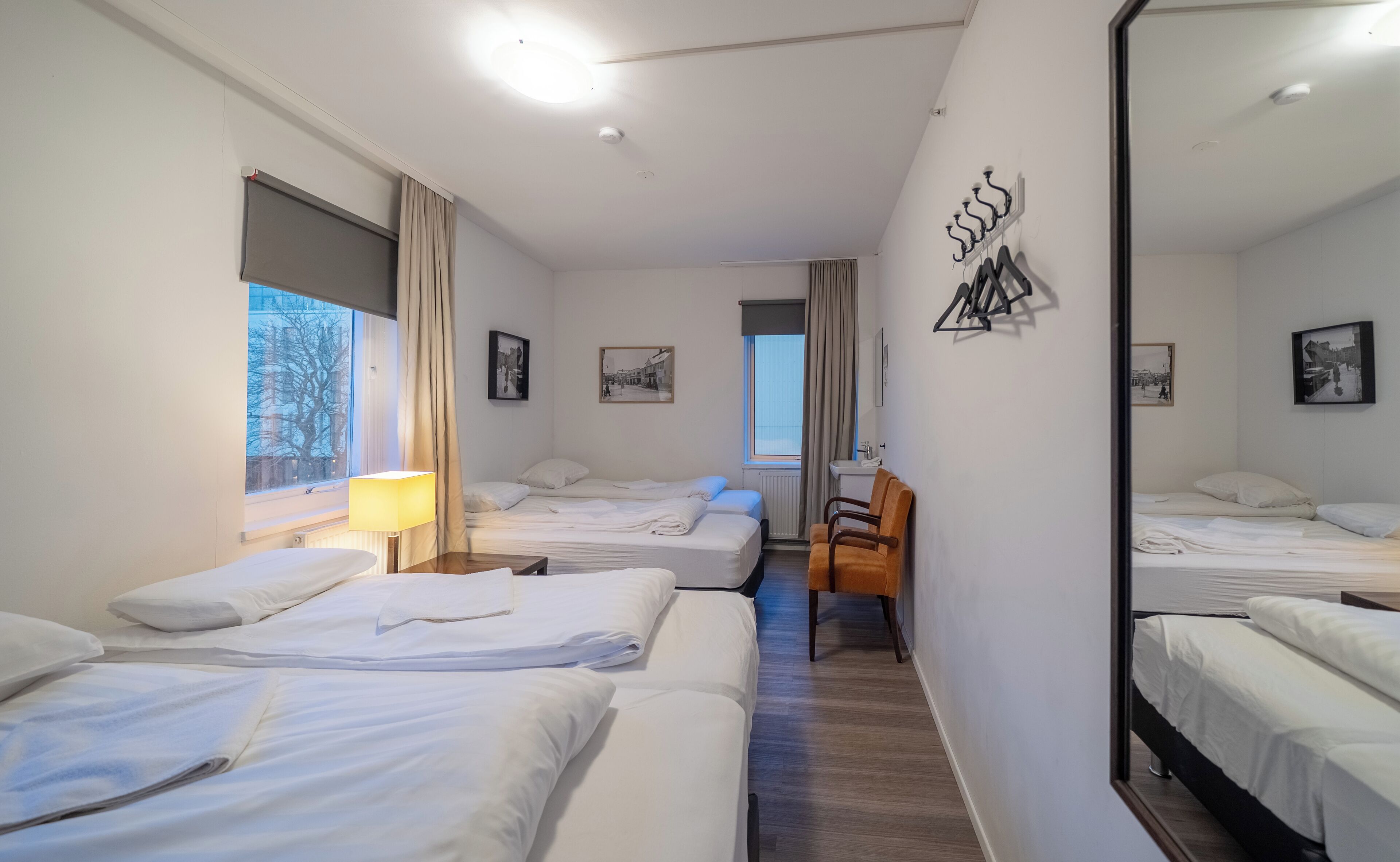 Quarto de hotel com três camas, um espelho grande e uma janela com cortinas.