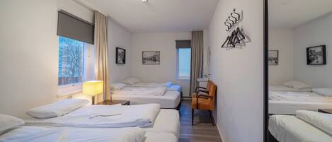 Quarto de hotel com três camas, um espelho grande e uma janela com cortinas.