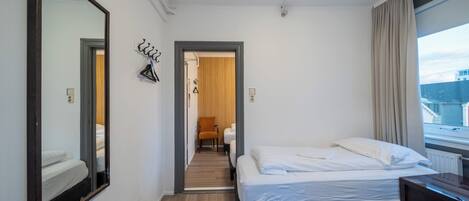 Habitación de hotel con dos camas, un espejo grande y vista a la ciudad.