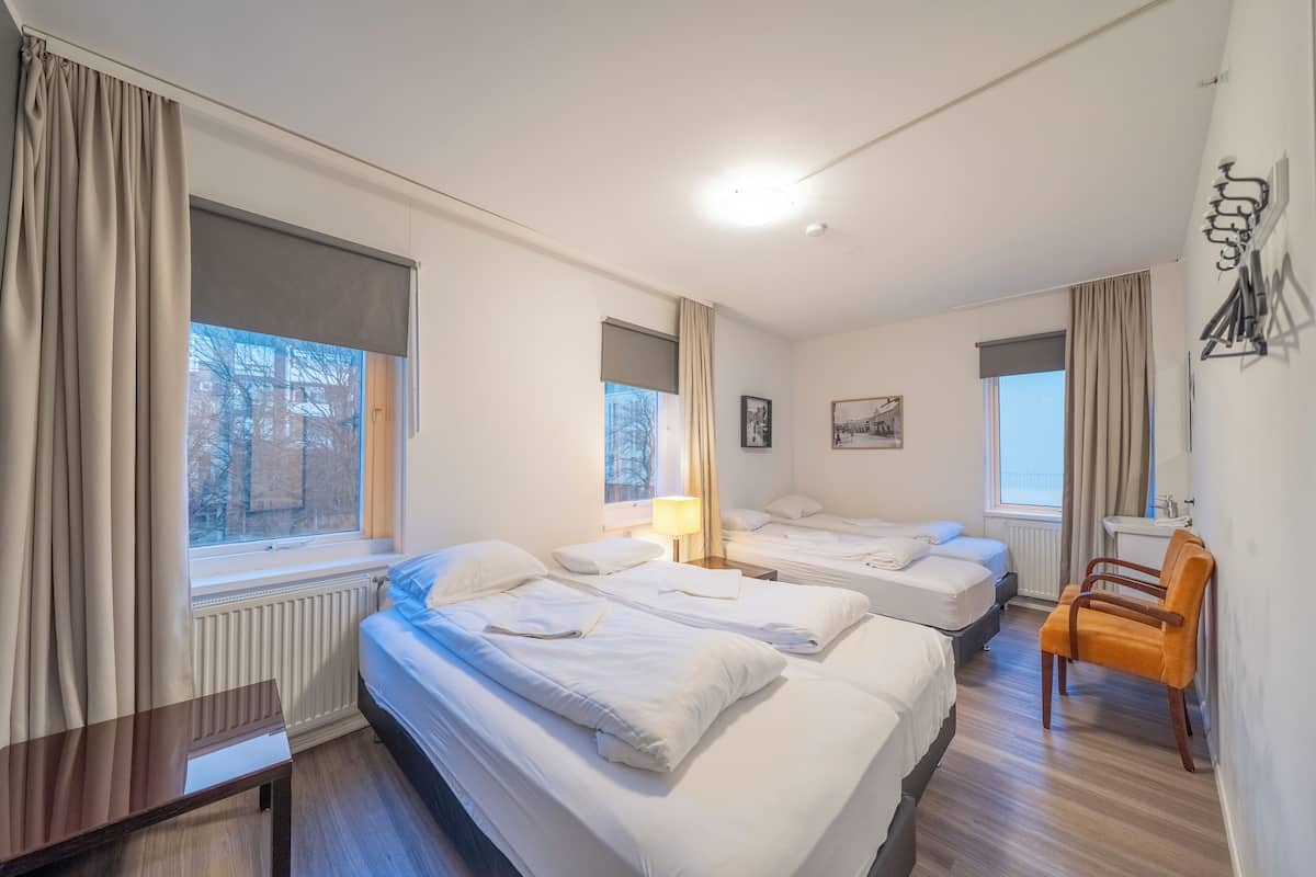 Hotellihuone, jossa on kaksi sänkyä, työpöytä, tuoli ja ikkuna, jossa on verhot.