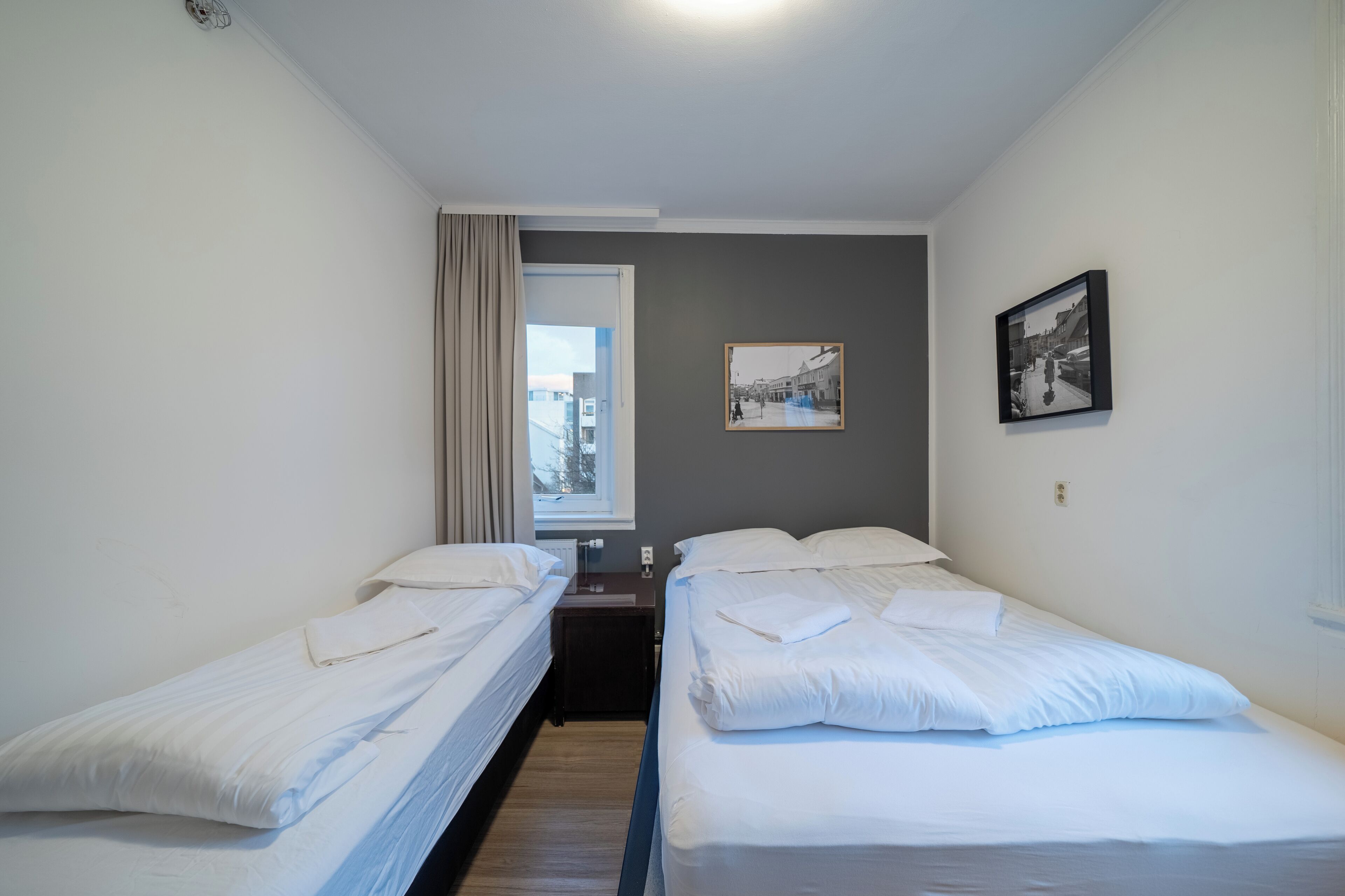 Een hotelkamer met twee enkele bedden, een raam met gordijnen, een kleine tafel en een aan de muur hangend schilderij.