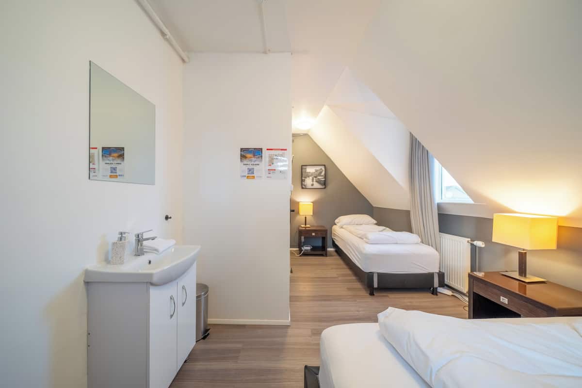Hotellihuoneessa on valkoinen pesuallas, sänky, yöpöytä lampun kanssa ja pieni yöpöytä lampun kanssa sekä taulu seinällä.