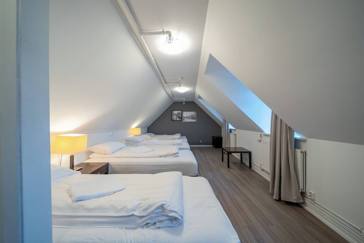 Hotellihuone, jossa on kolme sänkyä, työpöytä, tuoli ja kattovalaisin.